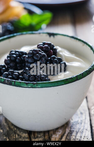 Sana colazione o brunch, preferito pasto mattutino con frutti di bosco. Yogurt freschi estate more nelle zone rurali la tazza sul tavolo di legno, close up, selettivo f Foto Stock