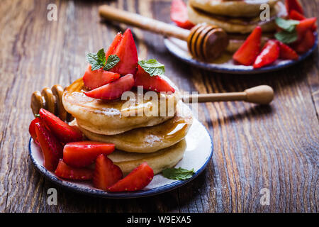 Sana colazione o brunch, preferito pasto mattutino. Frittelle fatte in casa, fresca estate le fragole con lo zucchero in polvere, miele su rurale tavolo in legno, cl Foto Stock