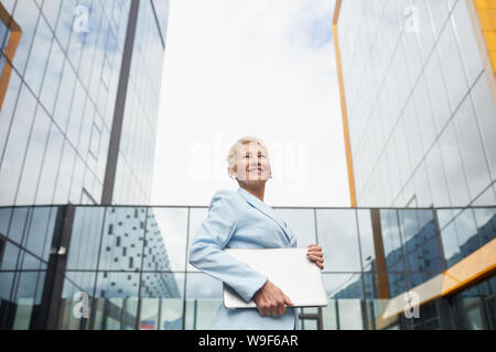 Ritratto di coppia imprenditrice bionda con i capelli corti e in abito elegante laptop holding e sorridente all aperto con un ufficio moderno edificio nel retro Foto Stock