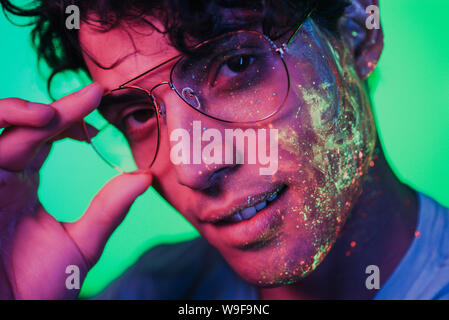 Bel ragazzo balli presso il rave party con dipinti fluorescenti sul suo volto Foto Stock