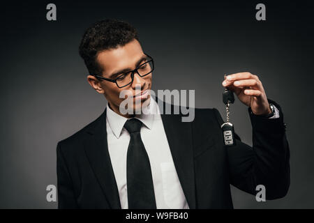 African American businessman guardando le chiavi dell'auto su sfondo scuro Foto Stock