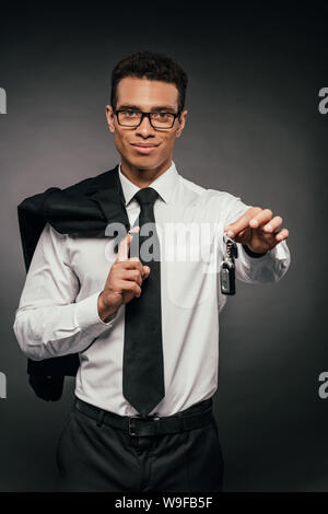 Sorridente African American businessman holding blazer e chiavi auto su sfondo scuro Foto Stock