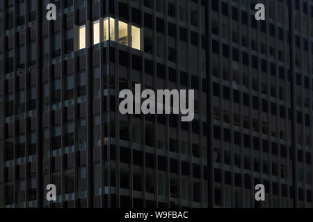 Angolo ufficio con le luci accese e windows incandescente nel buio di una costruzione di ufficio di notte che indica qualcuno lavoro straordinario a tarda notte Foto Stock