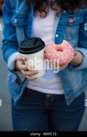 Mani tenendo una tazza bianca con dreank e rosa ciambella dolce in strada Foto Stock