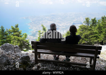 Un uomo e una donna seduti su una panchina affacciato sull'isola di Cefalonia e il Mar Ionio dalla cima del monte Ainos. Foto Stock