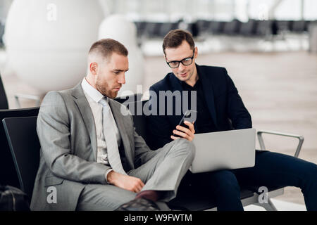 Giovane imprenditore che mostra un messaggio di testo sul suo telefono mobile ad un collega di sesso maschile in aeroporto Foto Stock