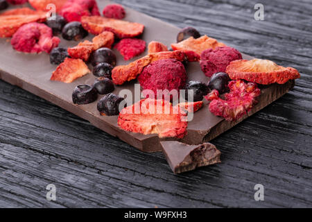 Cioccolato artigianale bar con frutti di bosco essiccati su un legno nero tabella. Macro shot. Vista frontale Foto Stock