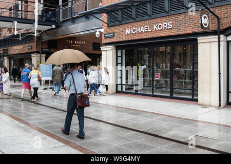 Un uomo si ripara dalla pioggia sotto un ombrello a un centro commerciale Foto Stock