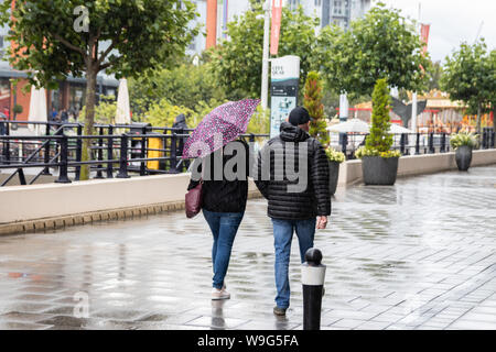 Un paio di camminare insieme sotto la pioggia la donna è in possesso di un ombrello Foto Stock