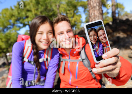 Selfie giovane utilizzando smart phone fotocamera prendendo foto Gite nella natura con lo smartphone. Coppia felice tenendo Self-portrait foto utilizzando app. L uomo e la donna per divertirsi insieme. Focus sullo schermo. Foto Stock