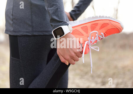 Esecuzione di stretching - runner indossa smartwatch. Primo piano delle scarpe da corsa, donna stretching gamba come warm-up prima di eseguire con attività di sport tracker guarda al polso per monitorare la frequenza cardiaca durante il cardio. Foto Stock