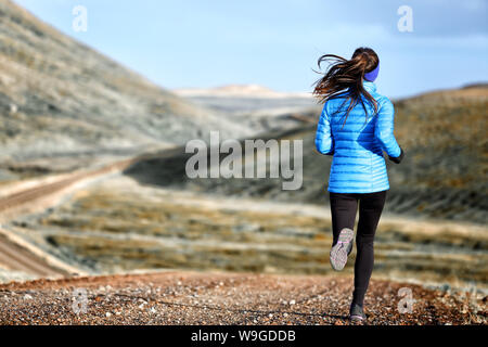 Donna autunno e inverno in esecuzione in down jacket. Esecuzione femminile jogging sul sentiero di montagna in un bellissimo paesaggio. Foto Stock