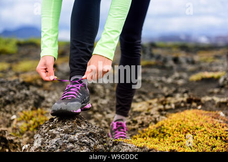 Trail runner donna ottenere pronto per eseguire sulla montagna rocciosa gara di fango in autunno. Atleta di vincolare il lacci delle scarpe da corsa. Primo piano delle mani. Foto Stock