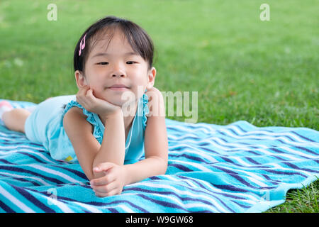 Poco toddler girl posa su asciugamano nell'erba su un giorno di estate Foto Stock