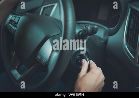 Primo piano interno veicolo della mano femminile in possesso della chiave di accensione. Donna di avviare il motore della macchina girando la chiave. Il volante e la femmina a partire automobile Foto Stock