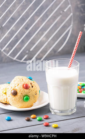 Un bicchiere di latte e biscotti decorati con colorate Jelly Beans caramelle uno sfondo grigio. Colazione per bambini snack. Foto Stock