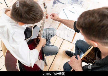 Uomo adulto spiega il suo figlio che impara a suonare la chitarra, come giocare a corda studiato correttamente. L'istruzione con la famiglia. Foto Stock