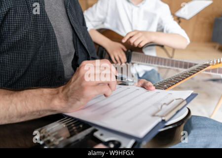 Uomo adulto spiega il suo figlio che impara a suonare la chitarra come suonare melodie e canzoni utilizzando il foglio di musica Foto Stock