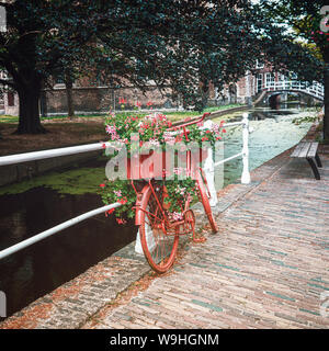 Bicicletta rosso decorato con granium attaccata alla ringhiera del Vrouwenregt Quay nel centro storico di Delft nei Paesi Bassi Foto Stock