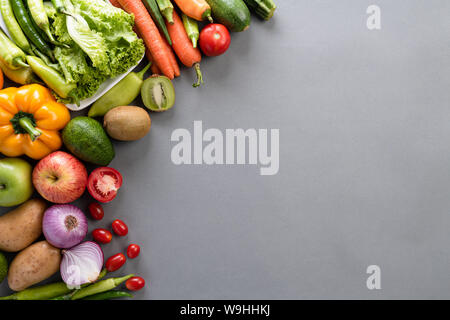 Uno stile di vita sano e concetto di cibo. Vista dall'alto di verdure fresche, frutta, erbe e spezie con un vuoto pastello rosa piastra su sfondo grigio. Foto Stock