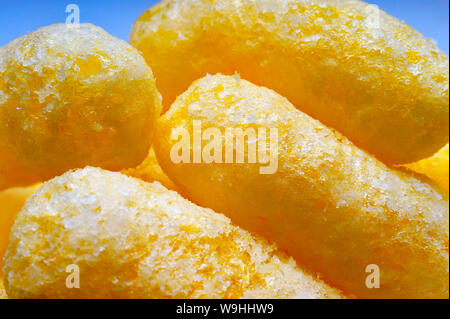 Close-up di arioso patatine di mais, bignè, Puffcorn spuntini su sfondo blu. Croccante soffiato aromatizzato pronto a mangiare prelibatezze. Partito, Cinema, TV, gioco S Foto Stock