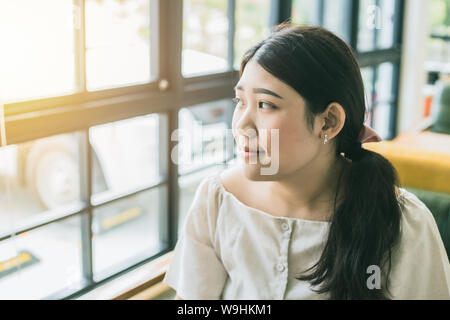 Felice bella giovani asiatici plus femmina dimensione chubby teen guardando fuori di windows per rilassarsi in cafe Foto Stock