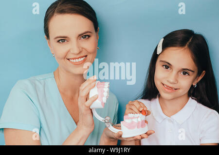 Sorridente razza mista ragazza con Dentista pediatrico che mostra di spazzolatura modo giusto la spazzolatura dei denti su sfondo blu Foto Stock