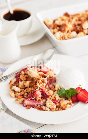 Strawberry crumble servito con gelato e fragole fresche e foglie di menta su bianco tavolo rustico Foto Stock