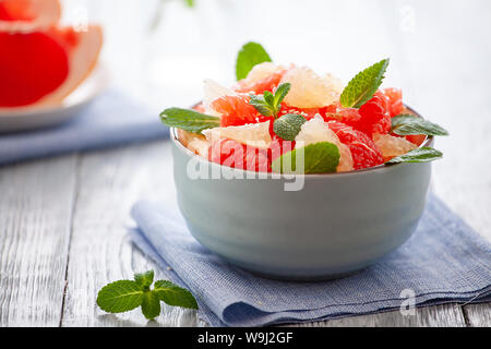 Insalata di pompelmo con le foglie di menta in una ciotola su un tovagliolo di lino e tavolo in legno .close-up Foto Stock