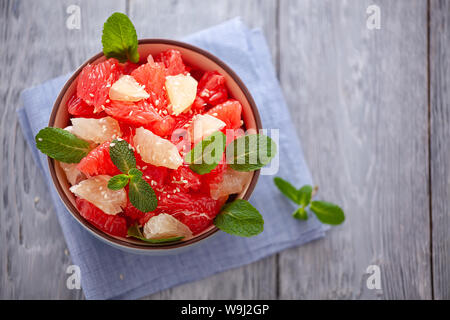 Insalata di pompelmo con le foglie di menta in una ciotola su un tovagliolo di lino e tavolo in legno .close-up, vista dall'alto. Foto Stock