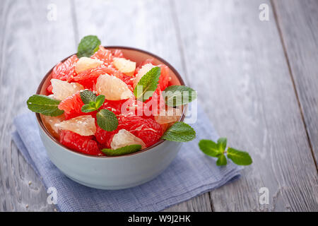 Un pompelmo insalata con le foglie di menta in una ciotola su un tovagliolo di lino e tavolo in legno .close-up. Foto Stock