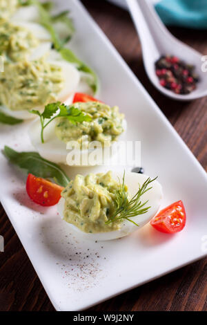 Deviled uova con purea di avocado e spezie decorate con le erbe aromatiche e i pomodori ciliegia Foto Stock