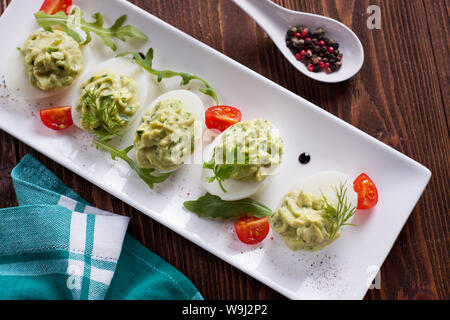 Deviled uova con purea di avocado e spezie decorate con le erbe aromatiche e i pomodori ciliegia Foto Stock