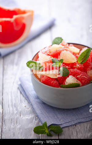 Insalata di pompelmo con le foglie di menta in una ciotola su un tovagliolo di lino e tavolo in legno . Foto Stock