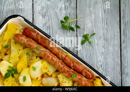 Tasy cotti fette di patate fritte con salsicce di Monaco di Baviera con le foglie di basilico su una placca da forno Foto Stock