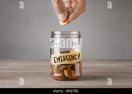 Emergenza. Vaso di vetro con monete e un iscrizione emergenza. Chi detiene moneta in mano Foto Stock