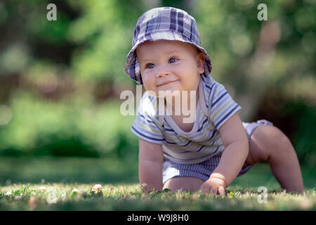 Bambino con bel tappo blu strisciando sul verde del prato in giardino Foto Stock