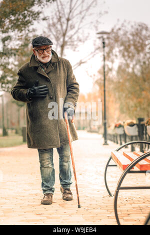 Un solitario senior uomo a camminare nel parco sperimentando dolore toracico Foto Stock