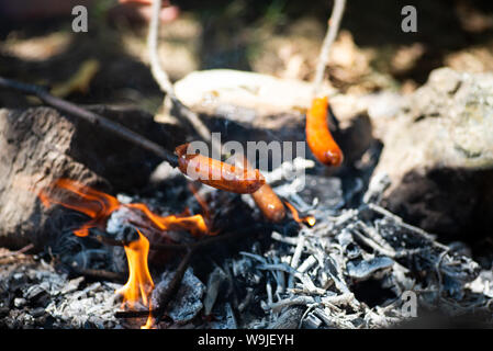 Persone salsiccia di cottura sul fuoco su un bastone ad un picnic Foto Stock