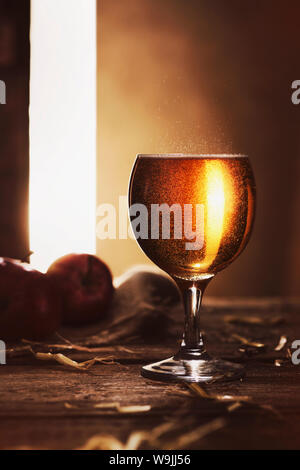 Bicchiere pieno di golden sidro su una tavola in legno rustico con la tarda sera sun proveniente tramite un gap in una porta. Foto Stock