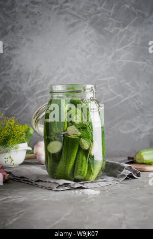 Il decapaggio e la fermentazione cetriolo in un barattolo di vetro con aneto e aglio sul grigio scuro del piano portapaziente in calcestruzzo. Foto Stock