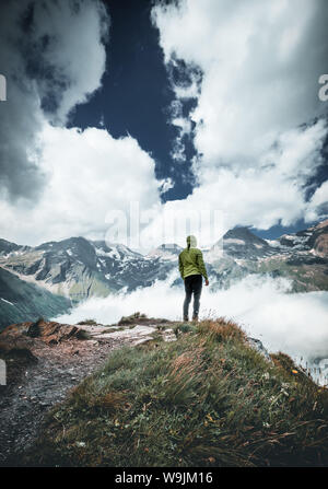 Ampio panorama di montagna. Piccole silhouette di persona sulla montagna rocciosa pendio coperto con il bianco puffy nuvole e nebbia. Foto Stock