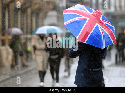 Un uomo cammina attraverso Cambridge che porta una bandiera europea ombrello, come Heavy Rain e temporali colpire parti della Gran Bretagna oggi. Foto Stock