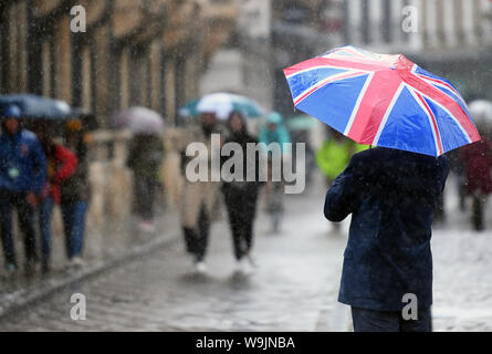 Un uomo cammina attraverso Cambridge che porta una bandiera europea ombrello, come Heavy Rain e temporali colpire parti della Gran Bretagna oggi. Foto Stock