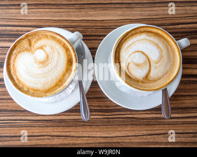 Due tazze di cappuccino con latte art su un tavolo di legno. Bellissima schiuma bianca, tazze di ceramica, il caffè del mattino Foto Stock