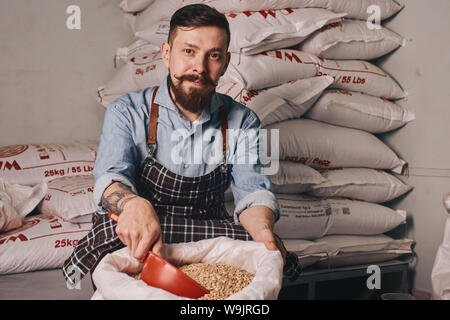 Ritratto di un barista professionale con il tatuaggio sul suo braccio al suo luogo di lavoro indossare un grembiule e denim shirt. Foto Stock