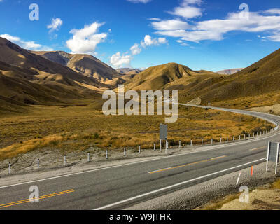 Lo stupefacente paesaggio marrone delle colline e delle montagne del Lindis Pass, Nuova Zelanda con una tessitura stradale attraverso il paesaggio nessuno in th Foto Stock