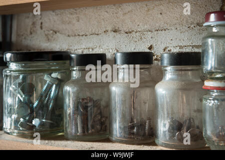 Righe di vetro riciclato vasetti contenitori utilizzati per memorizzare diverse dimensioni di viti, chiodi, barche, rondelle, dadi in modo organizzato Foto Stock