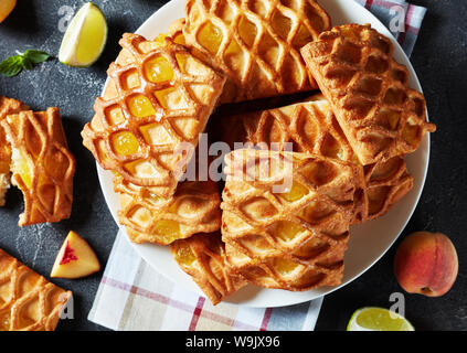 Pasta sfoglia mini torte con pesca e lime jam riempimento su una piastra bianca su una tabella di calcestruzzo con pesche fresche e fettine di lime, vista orizzontale da ab Foto Stock