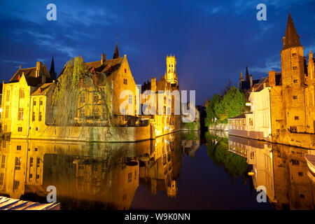 Il campanile e gli edifici illuminati di notte lungo un canale nel centro storico di Bruges, sito Patrimonio Mondiale dell'UNESCO, Belgio, Europa Foto Stock